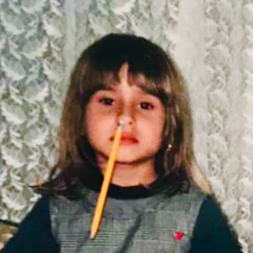 Photo of Mitra as a toddler with a pencil in her nose